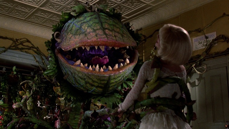 The towering green plant Audrey II grips innocent Audrey with its leafy appendage in "Little Shop of Horrors" (1986)