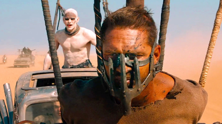 Max rides on a rig in front of a white-painted War Boy in 'Mad Max: Fury Road' (2015)