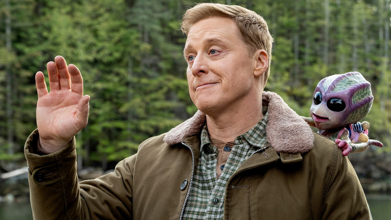 Harry waving with a small alien on his shoulder in "Resident Alien."