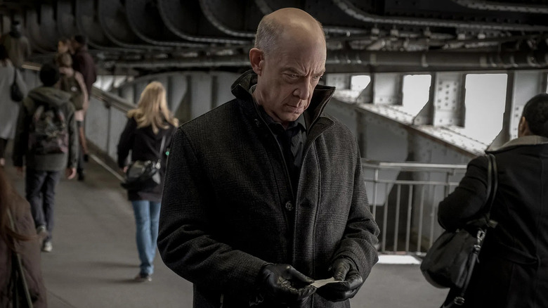 Howard Sillk walks through a train station while holding a small paper note and wearing a large black coat in "Counterpart"