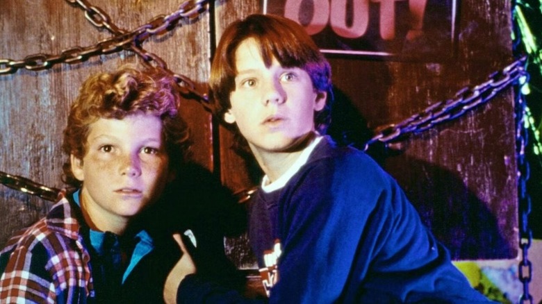 Marshall Teller holds his friend Simon Holmes as they crouch by a red door with metal chains around it in "Eerie, Indiana"