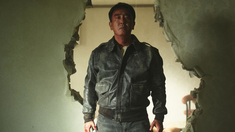 Jang Ju-won stands in front of a broken wall while wearing a black leather jacket in "Moving"