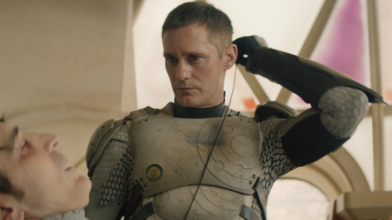 Murderbot wearing scuffed armor and plugging himself into Gurathin's (David Dastmalchian) biotech implant