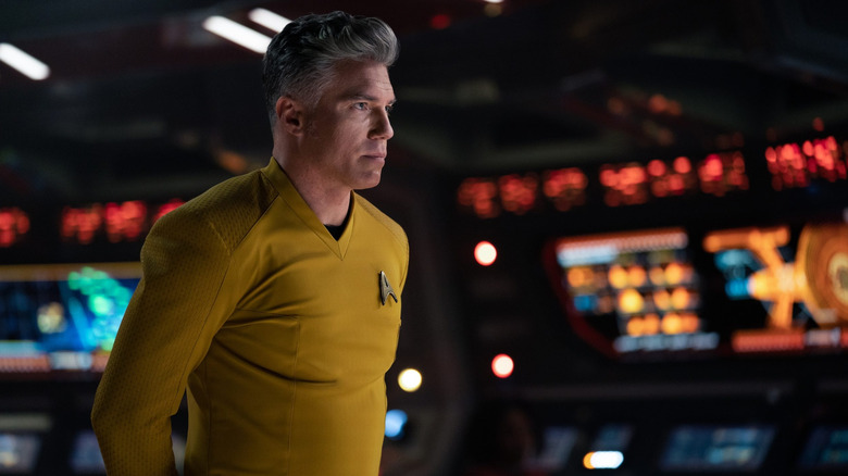 Captain Pike (Anson Mount) in his Star Fleet uniform standing on the Enterprise bridge with his hands behind his back