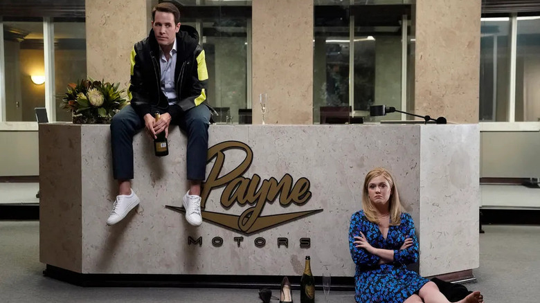 Wesley sitting atop the Payne Motors lobby desk while drinking with Sadie in American Auto