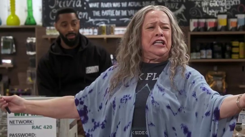 Ruth speaking and gesticulating while Carter watches from behind the dispensary counter in Disjointed