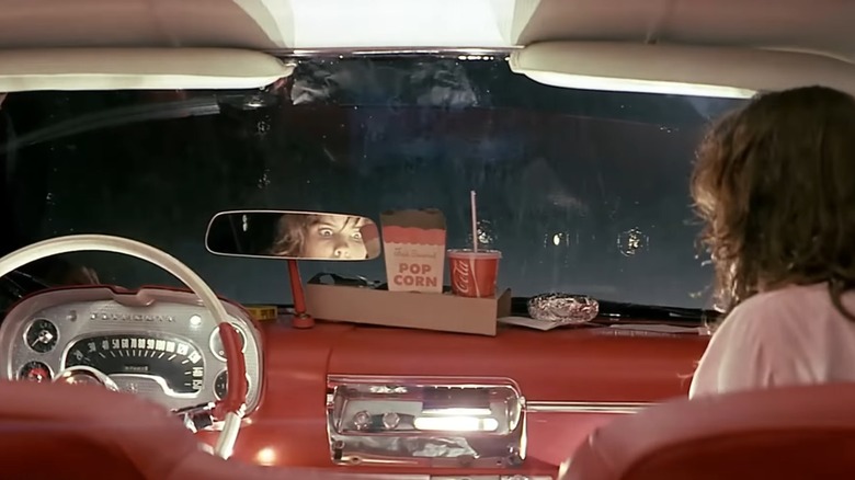 Leigh sitting in the passenger seat of the titular Christine, a car with an eerily-lit red leather interior