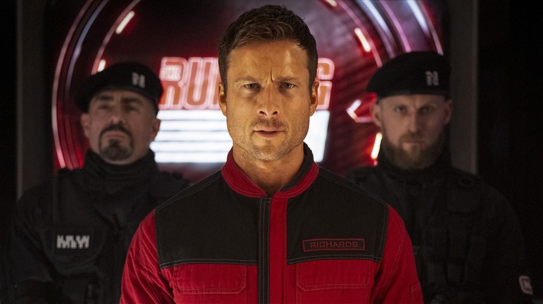 Ben Richards standing flanked by guards in 