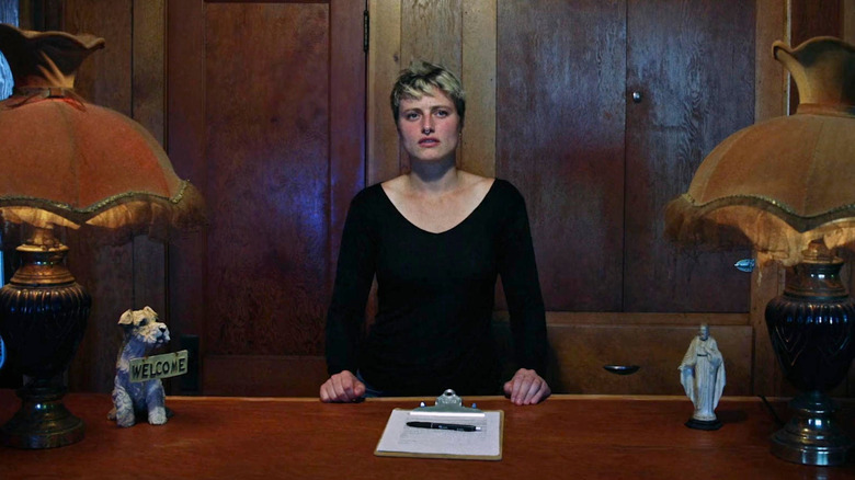 Ruthie stands at the reception desk in "Mother of Flies" (2025)