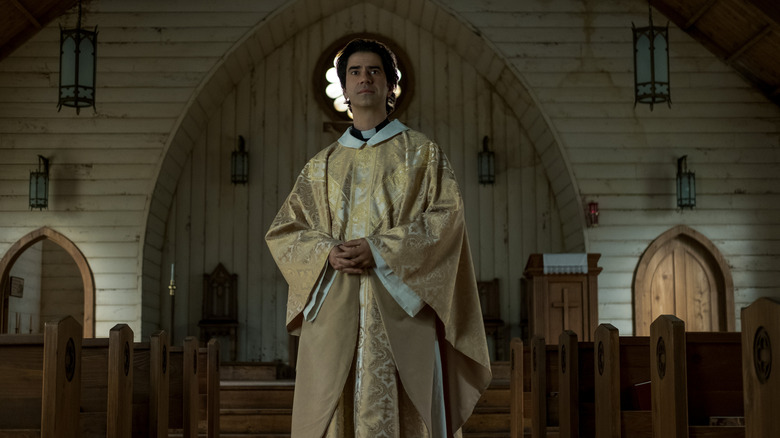 Father Paul standing ominously in church in Midnight Mass (2021)