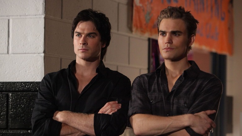 Damon and Stefan standing side by side with their arms crossed, wearing black, in The Vampire Diaries (2009)