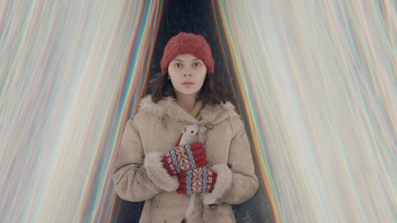 Lyra stands between two waves of light, holding a small ferret, in "His Dark Materials" (2019-2022)