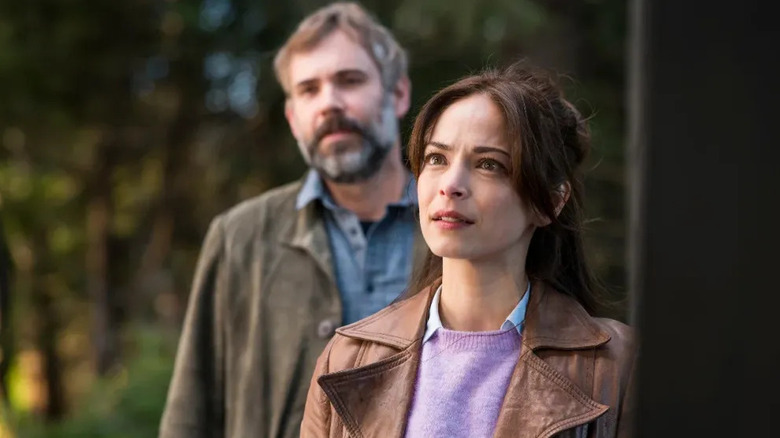Cassandra and Karl stand at a front door in Murder in a Small Town