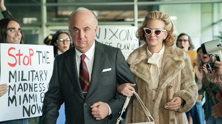 John and Martha walk forward while hounded by protestors and paparazzi.