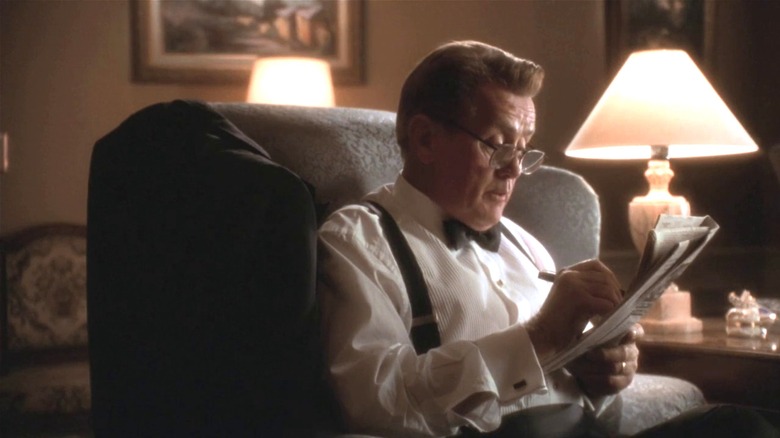 President Bartlet sits in a chair holding a newspaper.