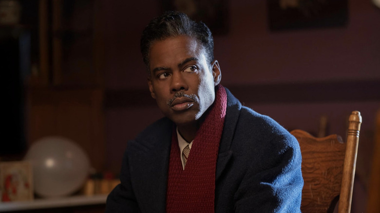Loy Cannon sitting on wooden chair in office in blue wool coat and burgundy scarf
