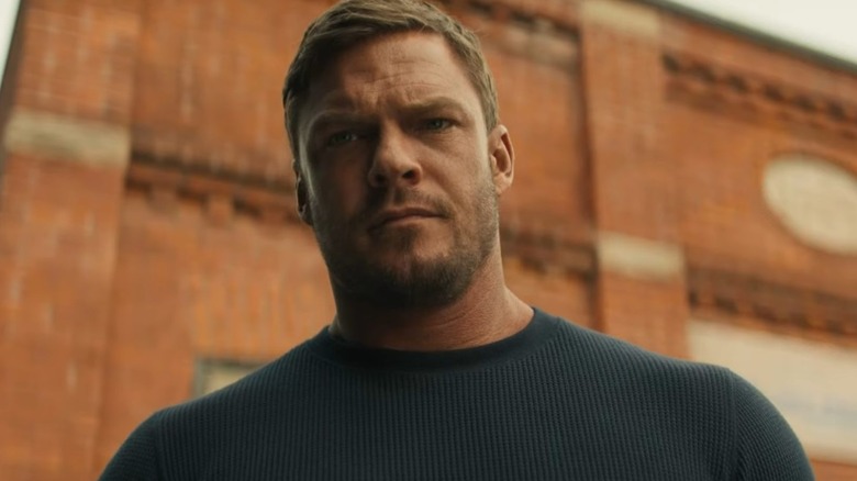 Reacher stands tall in front of an old brick building in Reacher.