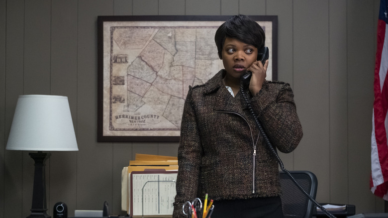 Tamika, in a woven jacket, answering phone in her office on Orange is the New Black