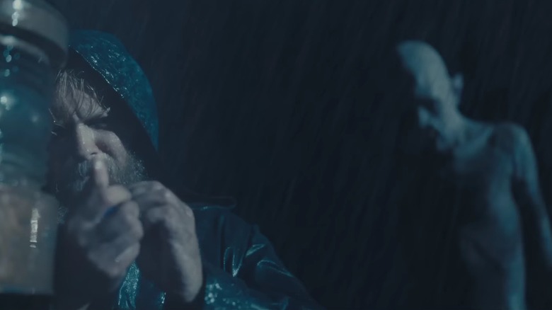 Larsen checks a lamp in the driving rain, while Dracula looms behind him, in The Last Voyage of the Demeter