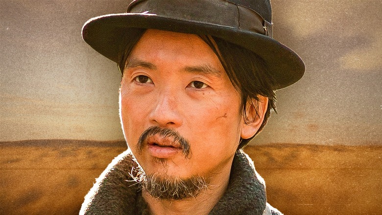 King-Lu standing in front of a background of a wide-open countryside in First Cow (2019)