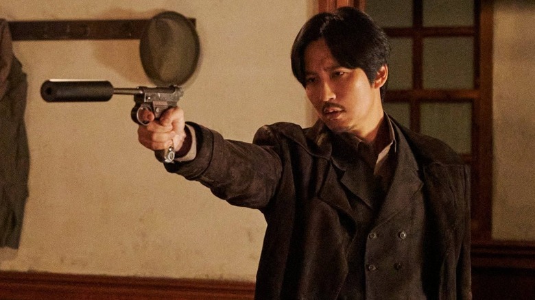 Lee pointing a gun with a silencer in "Song of the Bandits" (2023)