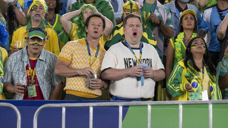 Elijah and Brad in the stands with green-painted fans in "Balls Up" (2026)
