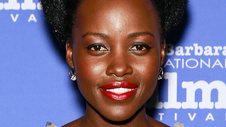 Lupita Nyong'o smiles against a blue background
