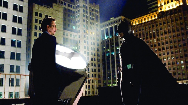 Commissioner Gordon and Batman standing next to the Bat-Signal in Batman Begins (2005)