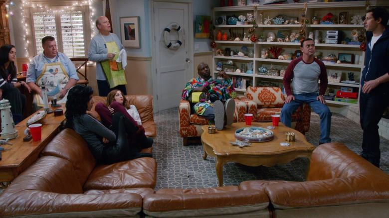 Jake standing in the beach house basement explaining to most of the squad.