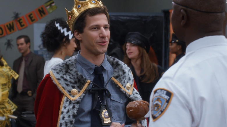 Jake (adorned in a crown and cape) talking smugly with Captain Holt at the precinct Halloween party