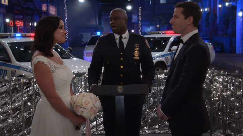 Amy and Jake, in traditional wedding garb, standing together at a makeshift wedding altar with Holt