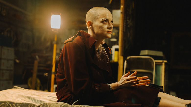 Michelle sits on a bed with her head shaved in "Bugonia" (2025)