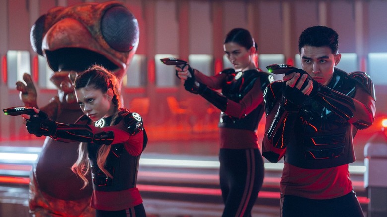 The lapling mascot stands behind Genesis Lythe, Darem Reymi, and unnamed Starfleet cadet as they aim their phasers in Star Trek: Starfleet Academy (2026)
