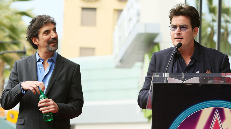 Chuck Lorre opens a soda while Charlie Sheen talks at a podium