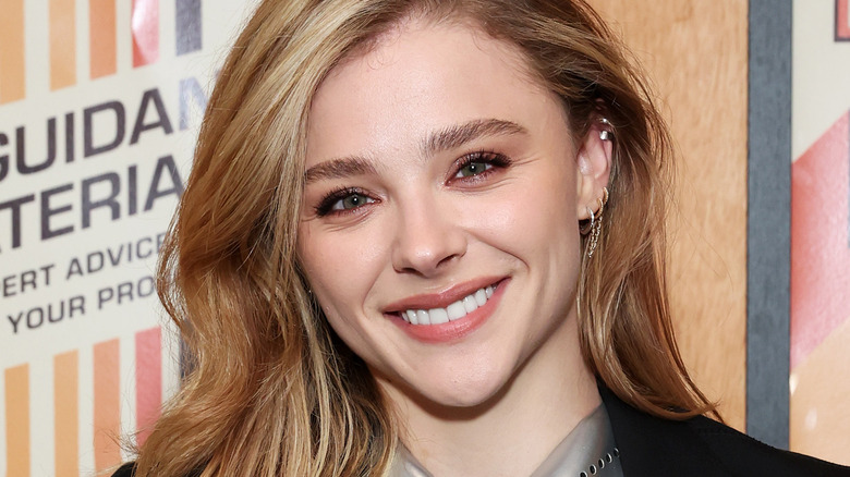 Chloe Grace Moretz smiles in front of promotional posters
