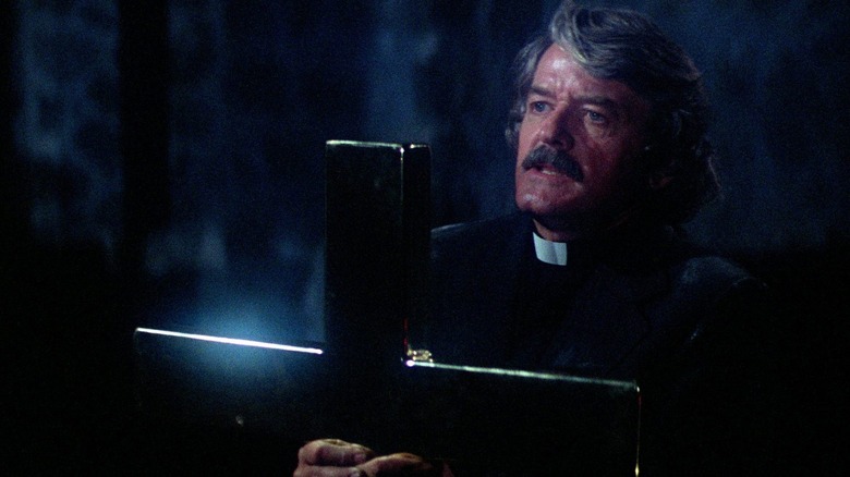 Father Patrick Malone holds up a cross in "The Fog" (1980)