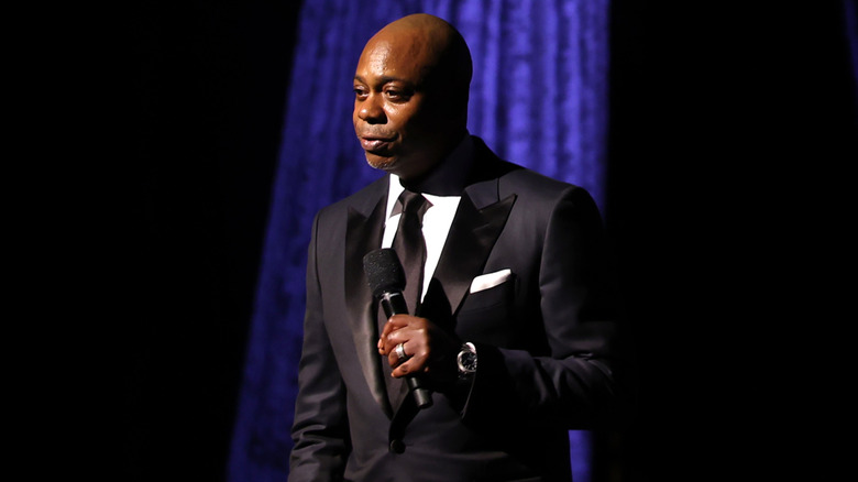 Dave Chappelle wearing a tux and holding a microphone