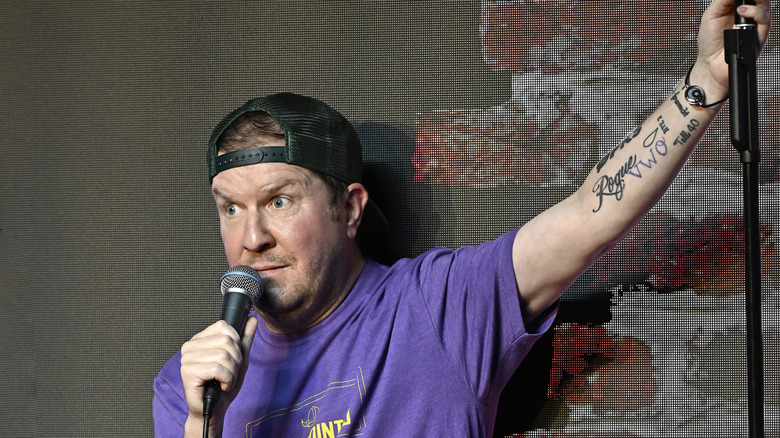 Nick Swardson with a backwards cap holding a microphine