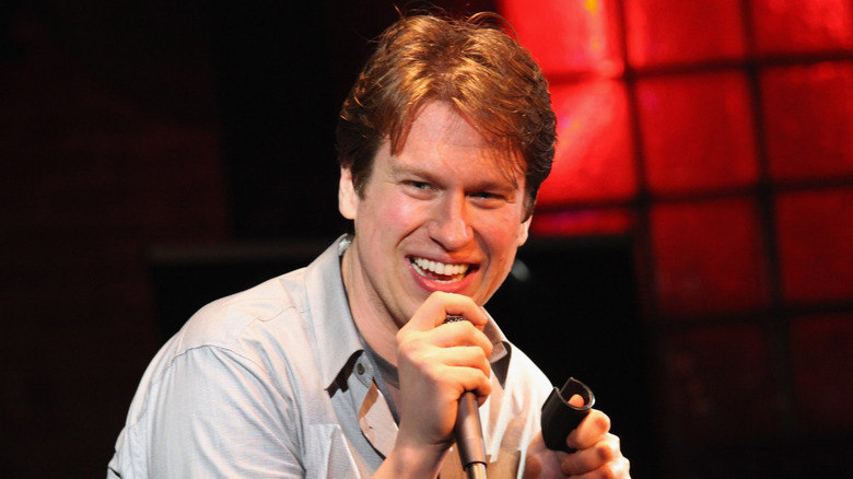 Pete Holmes holding a microphone and laughing