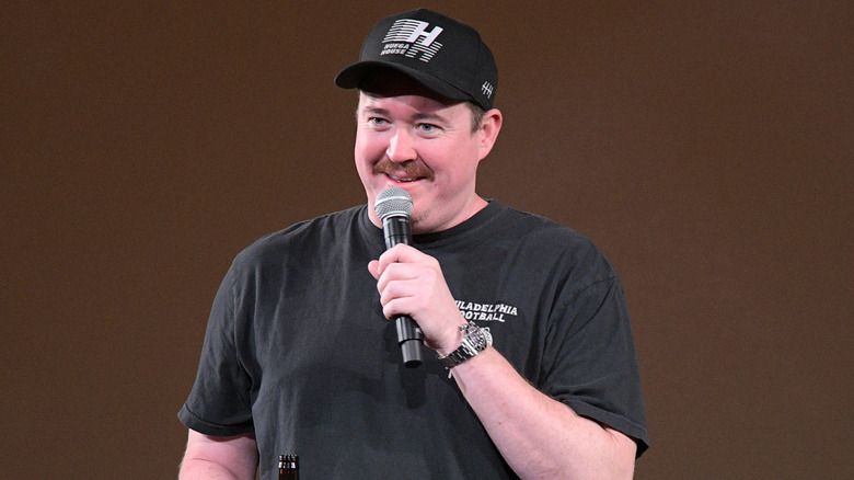 Shane Gillis in a black T-shirt and baseball cap