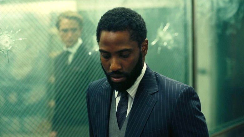 Niles standing behind a glass wall with a bullet hole behind The Protagonist in Tenet (2020)