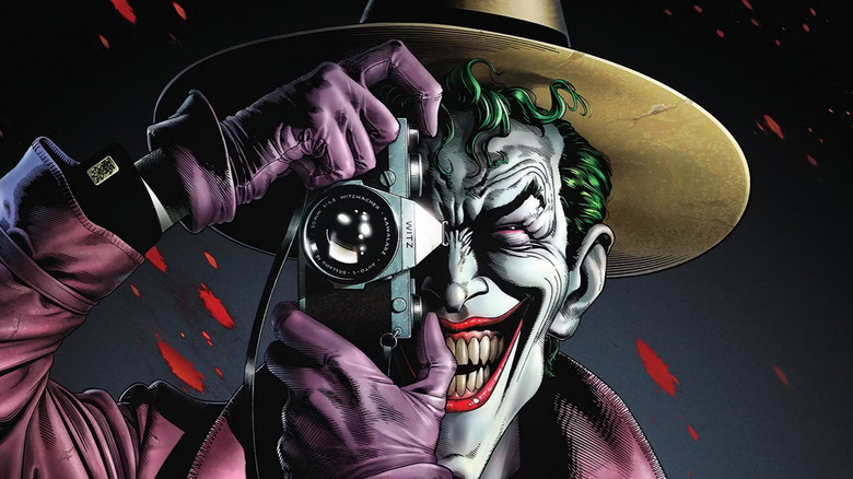 The Joker dressed in a hat, gloves, and trench coat, angling a camera as if to take a picture of the viewer