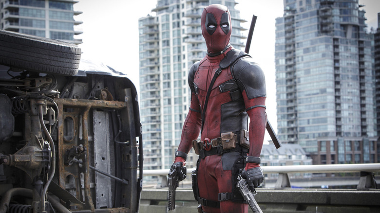 Deadpool in costume next to a flipped car