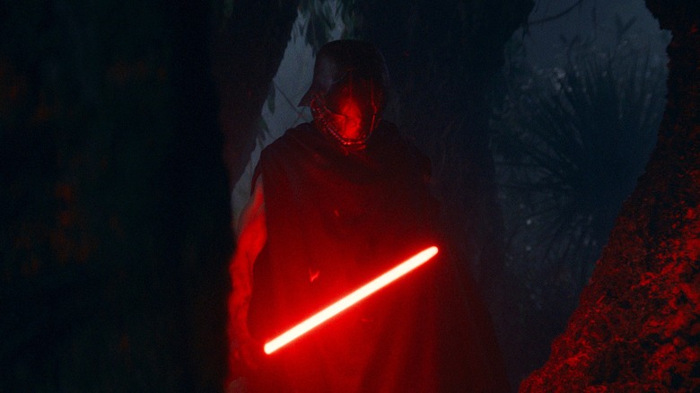 The Stranger stalking through a dark forest, illuminated by is red lightsaber, in Star Wars: The Acolyte