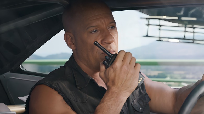 Dominic Toretto speaking on a walkie-talkie with a helicopter flying outside his car window