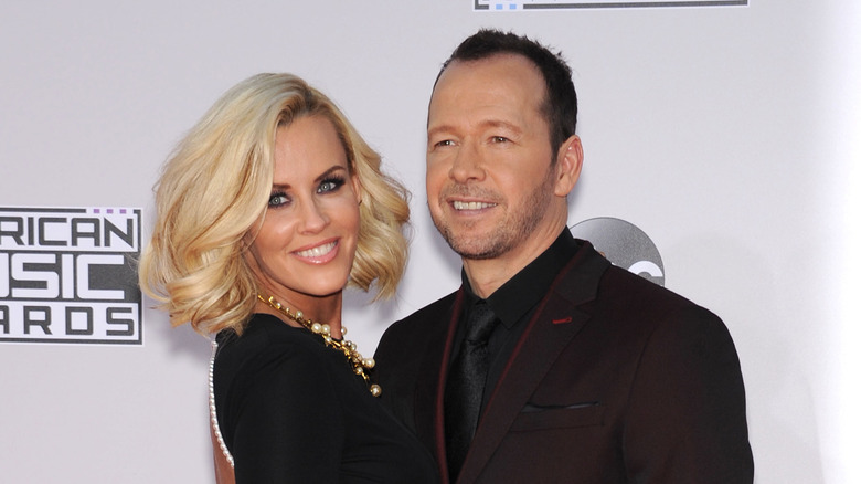 Donnie Wahlberg wearing dark red suit next to Jenny McCarthy in black dress