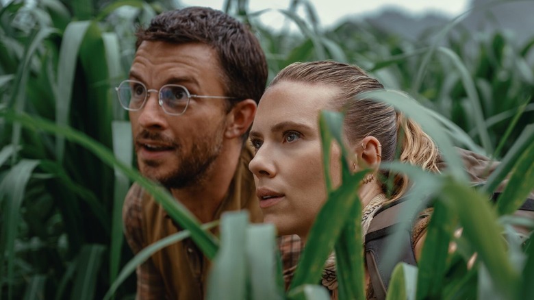 Dr. Henry Loomis and Zora Bennett hide in the grass in "Jurassic World Rebirth" (2025)