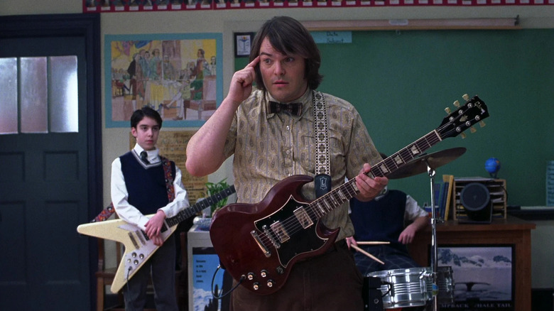 Dewey Finn points at his head and holds a guitar in "School of Rock" (2003)