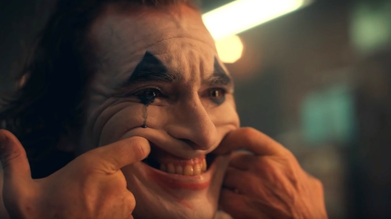 Arthur uses his fingers to stretch his face in "Joker" (2019)