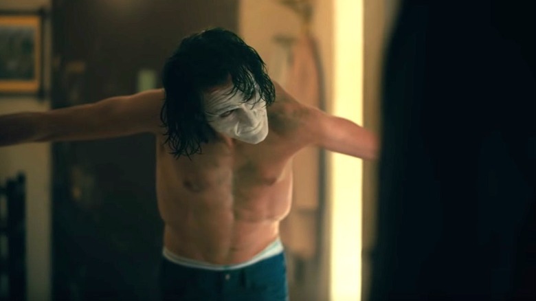 Joker poses shirtless but with makeup in front of the mirror in "Joker" (2019)
